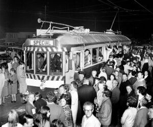 A crowd gathers around a vintage tram car labeled "SPECIAL" and numbered 40, with people looking out of the windows and standing on the platform at night.